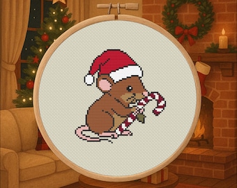 Op de afbeelding: Kruissteekborduurwerk van een bruine muis met een kerstmuts, die een zuurstok vasthoudt. De muis zit in een houten borduurring. De achtergrond toont een kerstboom, een open haard en een krans.