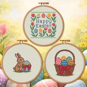 Puede incluir: Tres aros de bordado de punto de cruz con temas de Pascua. Uno dice "Happy Easter" rodeado de flores y huevos. Otro muestra un conejito marrón con un huevo de Pascua. El tercero representa una cesta de huevos decorados.