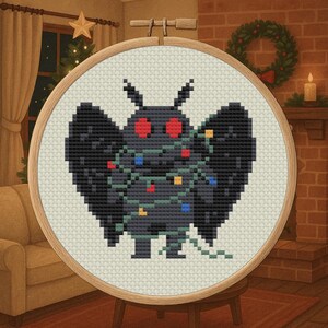 May include: Cross-stitch art of a black moth with red eyes, wrapped in Christmas lights. The artwork is set in a wooden embroidery hoop. The background shows a cozy Christmas scene with a fireplace, tree, and star.