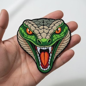 May include: Embroidered patch of a snake's head with an open mouth and fangs. The snake has green and beige scales, orange eyes, and a red and orange tongue. The patch is outlined in black.