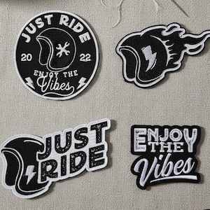 Może przedstawiać: Cztery czarno-białe naszywki z haftowanymi motywami motocyklowymi. Jedna naszywka jest okrągła z napisem "JUST RIDE" i "ENJOY THE VIBES". Inne naszywki przedstawiają kaski i błyskawice.