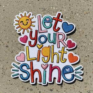 Könnte beinhalten: Gestickter Aufnäher mit dem Schriftzug "Let Your Light Shine" in bunten, verspielten Buchstaben. Das Design beinhaltet eine lächelnde Sonne, Herzen und ein Regenbogenschema, perfekt zum Aufnähen auf Kleidung oder Accessoires.