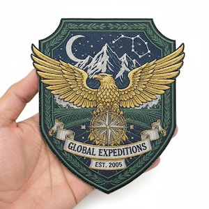 May include: Shield-shaped embroidered patch with a golden eagle, compass, and mountains under a starry night. The patch has the text "GLOBAL EXPEDITIONS EST. 2005" on a banner. The design is set against a dark green and navy blue background.