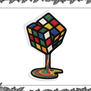 Op de afbeelding: Geborduurde patch met een kleurrijk Rubik's Cube-ontwerp. De kubus lijkt te smelten, waarbij de kleuren naar beneden stromen en een plas vormen. De patch heeft een zwarte rand en staat tegen een witte achtergrond.