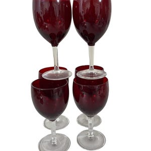 May include: A set of six wine glasses. The glasses have a deep red bowl and a clear stem and base. The glasses are arranged in a group, with some stacked on top of others.