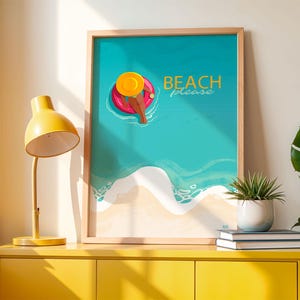 Puede incluir: Una impresión artística enmarcada con un tema de playa. La obra de arte representa a una persona relajándose en un flotador inflable rosa en el océano. Las palabras "BEACH please" están escritas en dorado. Una lámpara amarilla y una planta en maceta están sobre un mueble amarillo.
