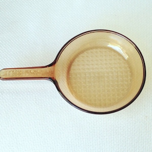 May include: A brown glass frying pan with a textured surface and a handle.