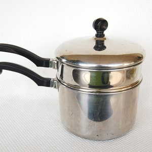 May include: Stainless steel double boiler with a lid and black handles. The pot has a shiny, reflective surface. The handles are curved and attached with silver rings. The lid has a black knob.