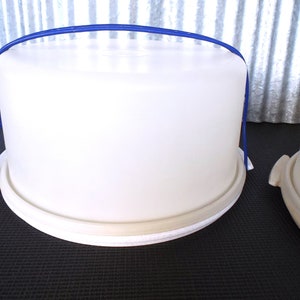 May include: White plastic cake carrier with a blue handle. The carrier has a white rim around the top and bottom.