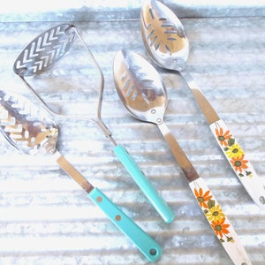 May include: Four kitchen utensils with turquoise and floral patterned handles. The utensils include a potato masher, a slotted spoon, and two ladles.