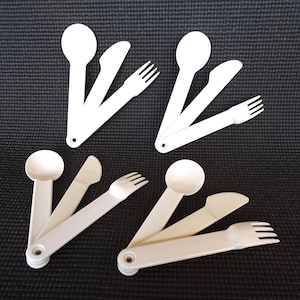 May include: Four white plastic utensils, including a spoon, knife, and fork, are arranged in two sets of three. Each set is folded together, with the spoon on top, the knife in the middle, and the fork on the bottom.