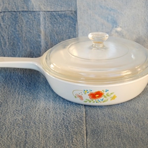 May include: White glass casserole dish with a lid and a floral design featuring red, yellow, and blue flowers. The dish has a white handle.