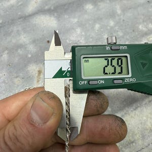 May include: A silver rope chain is measured with a digital caliper. The caliper displays a measurement of 2.59 mm. The chain is held by a hand with visible dirt.