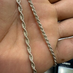 May include: Two silver-colored rope chains are displayed. The chains have a twisted design, with one chain slightly thicker than the other. The chains are shown against a skin-toned background.