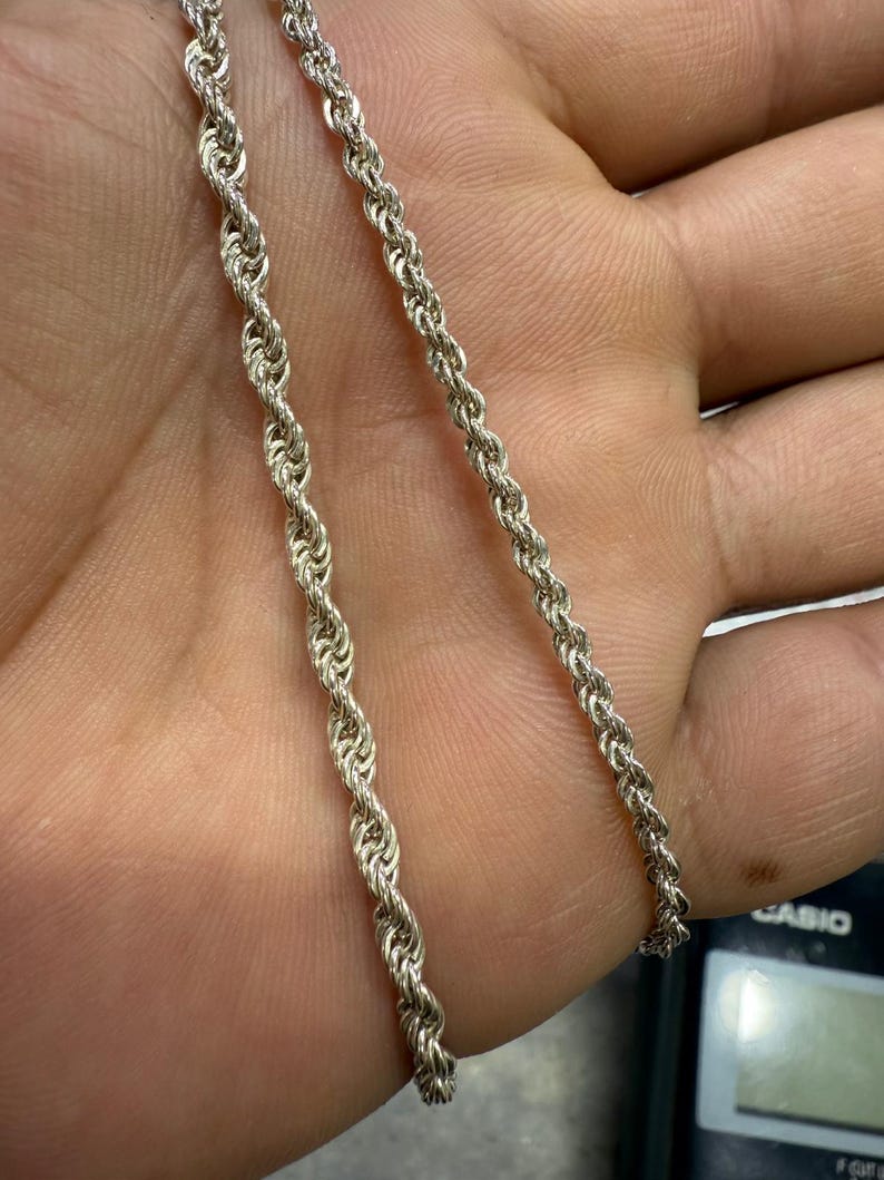 May include: Two silver-colored rope chains are displayed. The chains have a twisted design, with one chain slightly thicker than the other. The chains are shown against a skin-toned background.