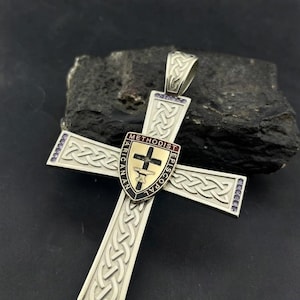 May include: A silver-toned cross pendant featuring intricate Celtic knotwork patterns and small purple stones at the tips. A central shield-shaped emblem displays the text "METHODIST EPISCOPAL" and a black cross with a chalice symbol in the center.