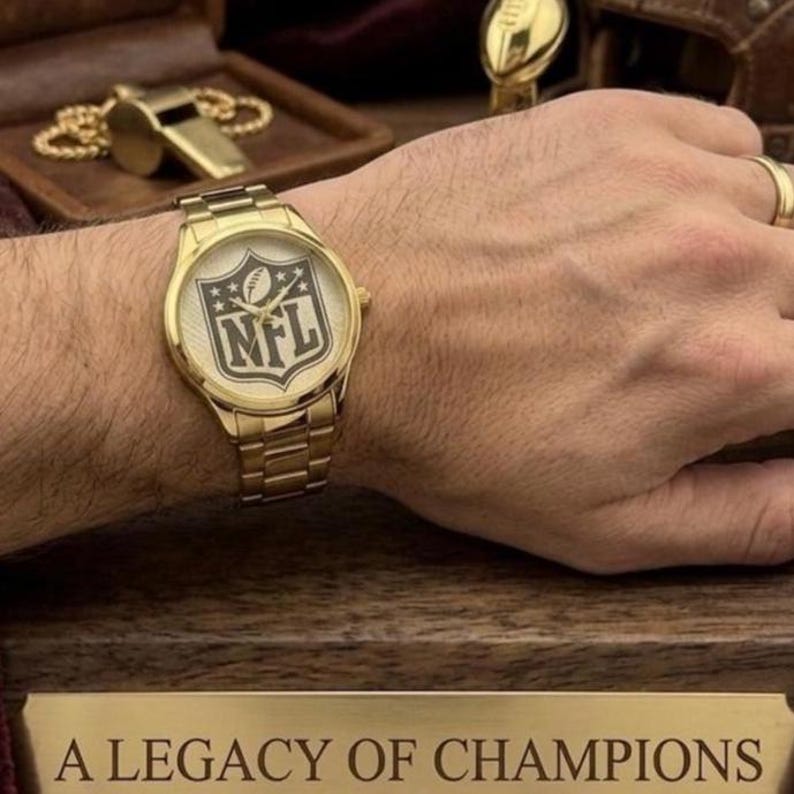 Puede incluir: Reloj de pulsera dorado con el logotipo de la NFL en la esfera. El reloj tiene una correa dorada y se muestra en una mu&ntilde;eca. La imagen tambi&eacute;n incluye un silbato dorado y el texto "A LEGACY OF CHAMPIONS".