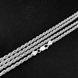 May include: Three silver rope chains with a lobster clasp, set against a dark background. The chains are made of twisted metal, reflecting light. The clasp is marked with "925".