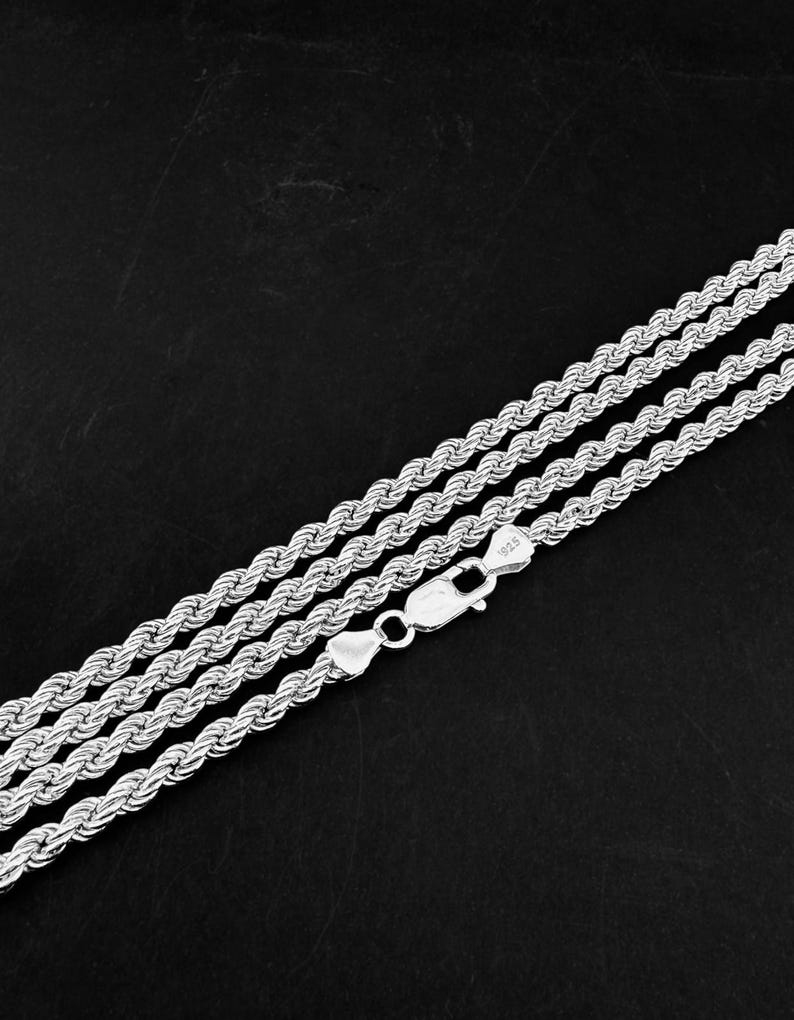 May include: Three silver rope chains with a lobster clasp, set against a dark background. The chains are made of twisted metal, reflecting light. The clasp is marked with "925".