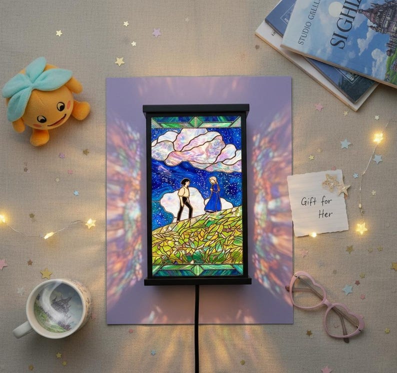 May include: A stained glass lamp with a black frame, depicting a couple on a hill under a starry sky. The lamp is on a purple background, with a plush toy, a mug, and a note that says "Gift for Her".