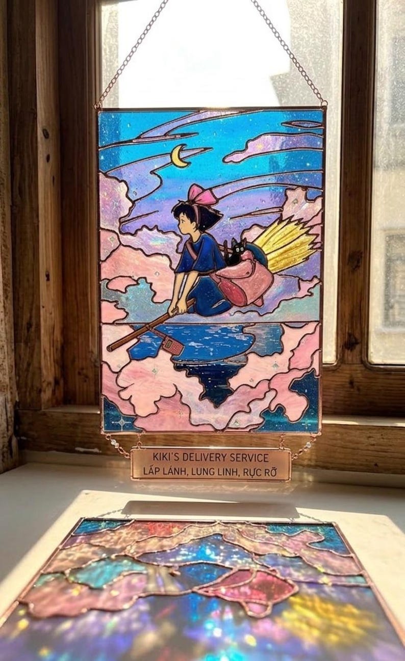 May include: Stained glass panel featuring a young girl on a broomstick, flying through a night sky with a crescent moon. The panel has a pink, blue, and purple color scheme, with the text "Kiki's Delivery Service" at the bottom.