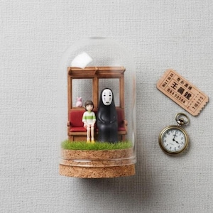 Puede incluir: Diorama en miniatura dentro de una c&uacute;pula de cristal con personajes de una pel&iacute;cula de animaci&oacute;n japonesa. La escena incluye un vag&oacute;n de tren, figuras y una base de corcho. Un reloj de bolsillo y un billete est&aacute;n al lado.