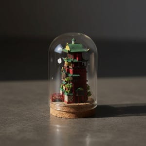 May include: A miniature red and green pagoda model inside a clear glass dome. The pagoda has multiple levels with green roofs and intricate details. The dome sits on a cork base, creating a decorative display.
