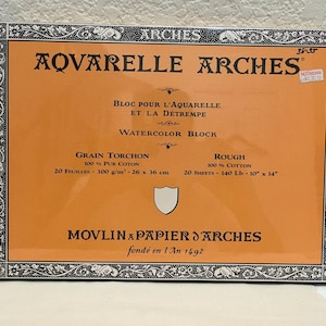 Pode incluir: Um bloco de aquarela laranja e preto da Arches. O bloco apresenta o texto "AQVARELLE ARCHES" e "WATERCOLOR BLOCK". Contém 20 folhas de papel 100% algodão, medindo 26 x 36 cm. O bloco é rotulado como "ROUGH".