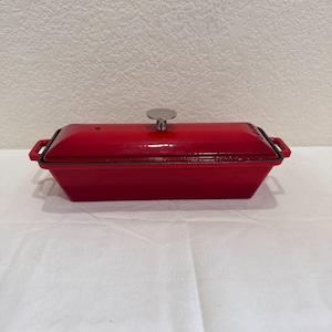 May include: A rectangular, red enameled cast iron Dutch oven with a matching lid. The lid has a silver-colored handle. The oven has two small handles on the sides. This cookware is suitable for baking, braising, and roasting.