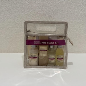 May include: A clear, zippered cosmetic bag containing four bottles of aromatherapy products. The bottles are labeled "REMEDIES PMS RELIEF KIT". The bag is beige with a clear front and a handle at the top.