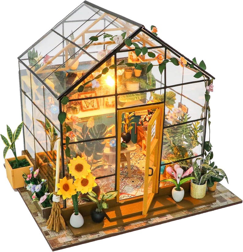May include: Miniature greenhouse model with glass walls and a pitched roof. The interior is filled with tiny plants, flowers, and furniture. The open door reveals a glimpse of the interior, illuminated by a warm light. Decorative vines and flowers adorn the exterior.