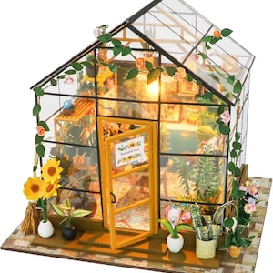 May include: A miniature greenhouse model with a glass roof and walls, featuring a wooden frame and door. The interior is filled with miniature plants, flowers, and decorative items. The exterior is adorned with artificial vines and flowers. The door has a sign.