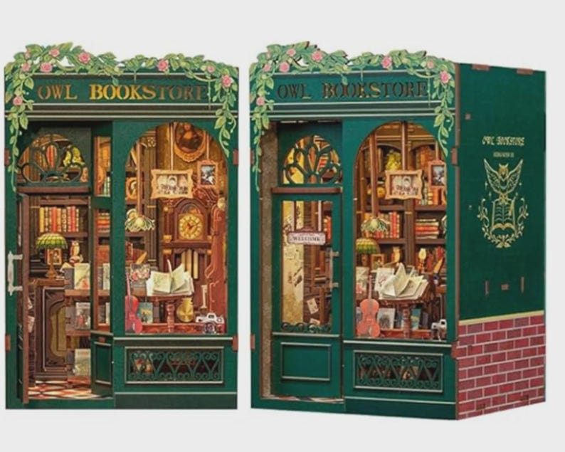 K&ouml;nnte beinhalten: Zwei Miniaturmodelle der Owl Bookstore. Die Fassaden sind dunkelgr&uuml;n mit floralen Akzenten und den Worten "OWL BOOKSTORE" &uuml;ber den T&uuml;ren. Die Innenr&auml;ume sind mit winzigen B&uuml;chern, Uhren und Lampen gef&uuml;llt. Eines hat einen roten Ziegelsockel.
