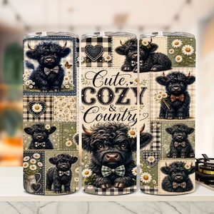 May include: A cylindrical tumbler featuring a patchwork design of black Highland cattle calves, white daisies, and black-and-white buffalo plaid patterns. The center text reads "Cute, COZY & Country" in a decorative black script and serif font.