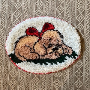 May include: Oval-shaped rug featuring a sleeping puppy with a red bow. The puppy is brown with a white and green border. The rug is made of a soft, textured material, perfect for a child's room or nursery.
