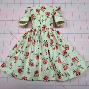 May include: A light green dress with a floral pattern of pink roses. The dress has a gathered skirt and puffed sleeves. It has a button closure down the back.