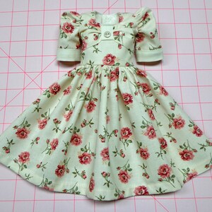 May include: A white dress with a floral pattern of pink roses. The dress has puffed sleeves and a gathered skirt.
