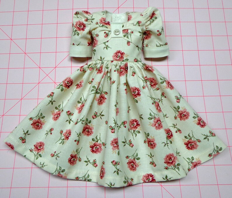 May include: A white dress with a floral pattern of pink roses. The dress has puffed sleeves and a gathered skirt.