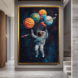 May include: A framed artwork depicts an astronaut floating in space, holding a cluster of colorful planet-shaped balloons. The planets include orange, blue, and green spheres against a dark blue and black starry background. The artwork is framed in gold.