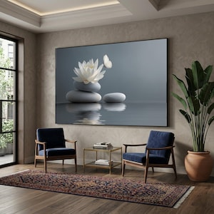 Peut inclure: Une grande œuvre d'art encadrée représente une scène sereine de pierres grises empilées, une fleur de lotus blanche et un papillon se reflétant dans l'eau. Deux fauteuils bleu marine avec des cadres en bois et un tapis à motifs complètent l'intérieur.