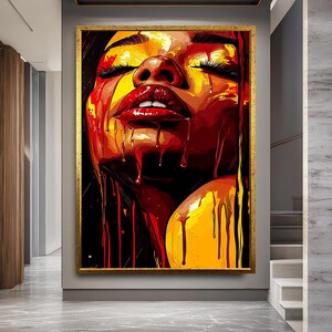 May include: A framed art print depicting a woman's face with closed eyes and red lips. The artwork uses red, yellow, and black, with dripping paint effects. The frame is gold. The artwork is displayed in a hallway.