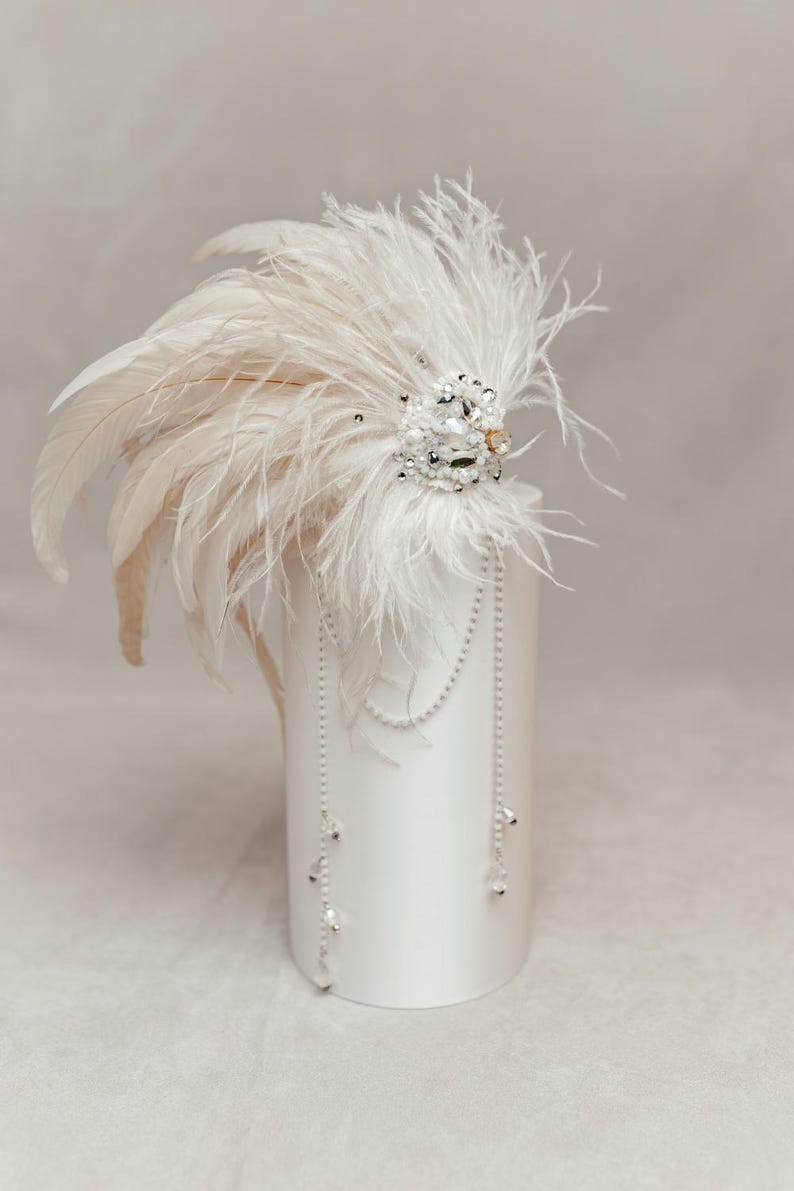 Boho-inspired feather headdress perfect for music festivals, bohemian weddings, or nature-themed photo shoots. Handmade with soft white ostrich feathers and natural rooster feathers, adorned with delicate pearls, crystals, and lace for a dreamy, earthy vibe. This lightweight and expressive headpiece adds artistic flair to any outfit. Displayed on a neutral mannequin head to highlight its flow, texture, and intricate handcrafted details under soft lighting.