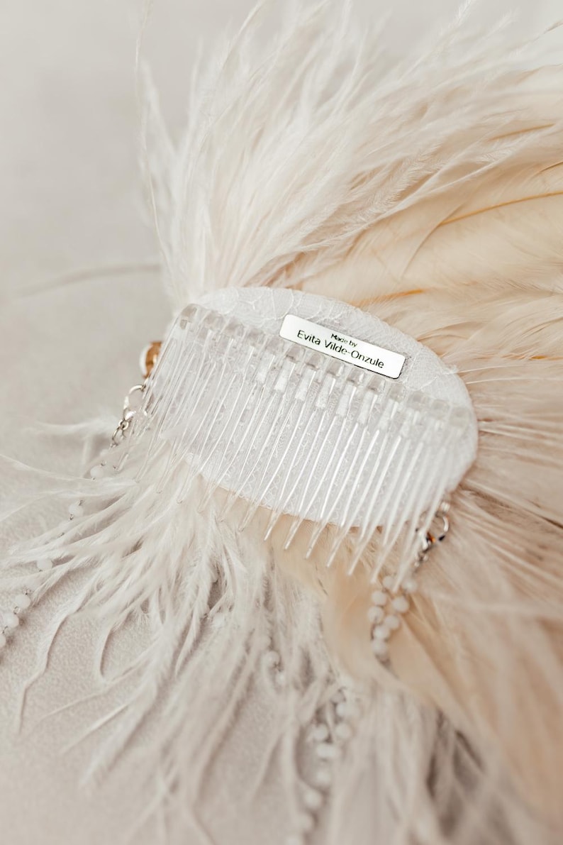 Elegant handmade feather headdress inspired by the Great Gatsby era, featuring soft white ostrich and dramatic rooster feathers. Embellished with pearls, lace, and sparkling crystals, this bridal headpiece adds a vintage, boho-chic touch to any wedding, festival, or photoshoot. Displayed on a white mannequin, the piece showcases fine craftsmanship, ideal for brides, performers, or themed events. Perfect as a wedding fascinator or statement hair accessory.