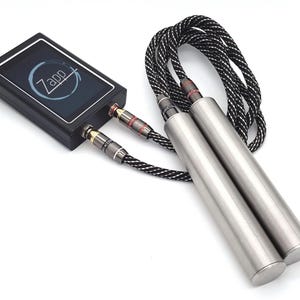 May include: A black rectangular electronic device with a screen displaying the text Zapp inside a circular graphic. Two black and white braided cables connect the device to two smooth, cylindrical, metallic handles with dark grey accents.