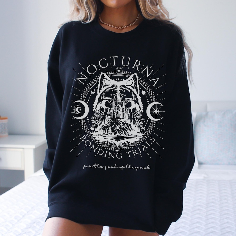 May include: Black sweatshirt with a white graphic featuring a wolf, castle, and crescent moons. The text reads "NOCTURNA BONDING TRIALS" and "for the good of the pack."