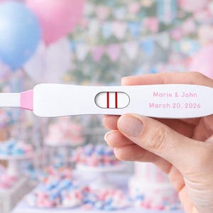 Puede incluir: Un test de embarazo blanco con detalles rosas y dos líneas rojas, sostenido en una mano. El test lee "Marie & John, 20 de marzo de 2026". El fondo presenta globos y pasteles, sugiriendo una fiesta de bienvenida al bebé o revelación de género.