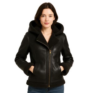 May include: A black leather jacket with a hood and a shearling lining. The jacket has a zipper closure and pockets. The cuffs and hem are trimmed with shearling. The model is wearing the jacket.