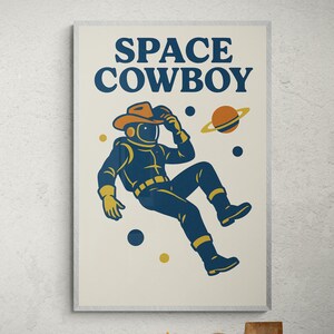 May include: A framed print featuring a retro illustration of a space cowboy. The artwork depicts an astronaut in a spacesuit and cowboy hat, with the words "SPACE COWBOY" above. The color palette includes navy blue, orange, and yellow.