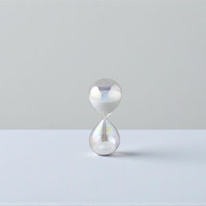 Può includere: Una clessidra iridescente con finitura perlata. Il recipiente di vetro è riempito di sabbia bianca e il design è a forma di goccia classica. La clessidra è un oggetto decorativo, perfetto per una scrivania o una mensola.