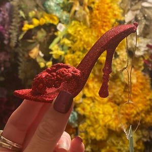 May include: A red glitter high heel shoe ornament with a small blue star hanging from it.